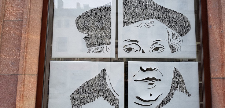 Man sieht als Grafik den Kopf von Martin Luther, unterteilt in vier puzzleähnliche Teile, als Bild an einer Wand